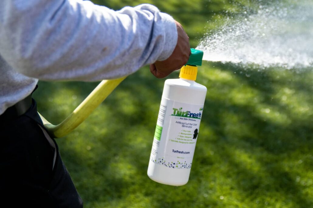 "A person spraying TurFresh turf deodorizer onto artificial grass, showcasing its powerful pet odor elimination, non-toxic formula, and eco-friendly ingredients safe for pets and families."