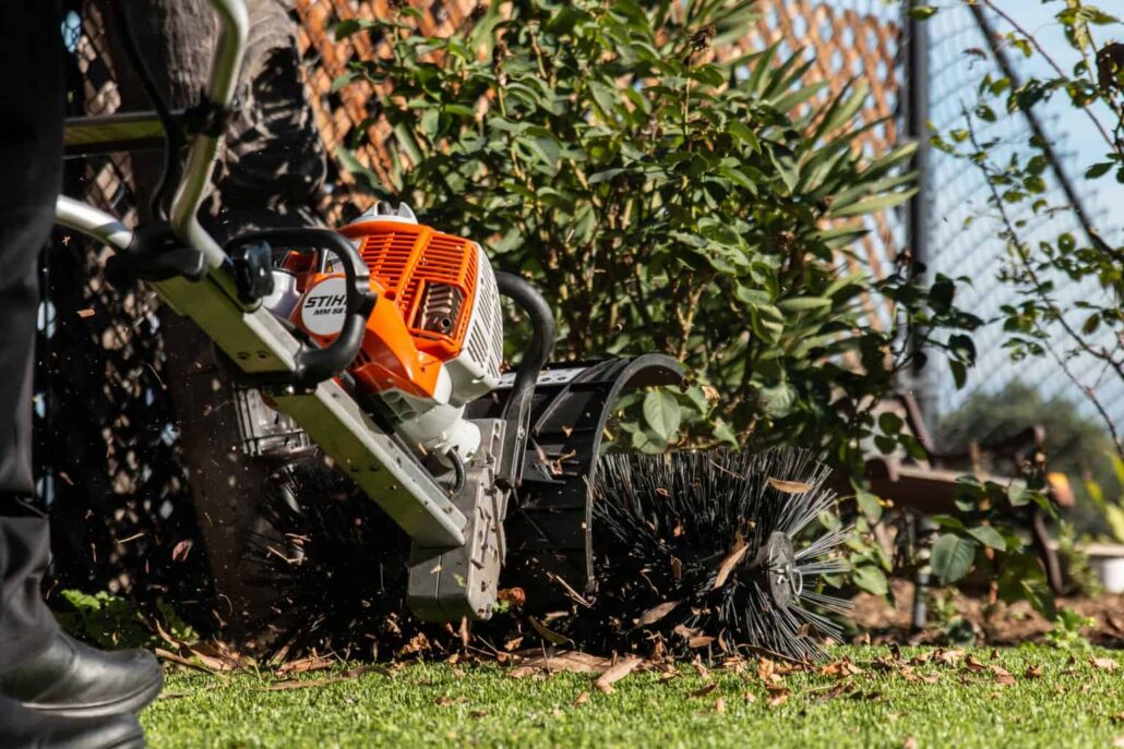 Power brush machine in action on artificial turf near garden bushes, illustrating TurFresh’s deep-cleaning service that removes debris, eliminates odors, and uses a non-toxic, pet-safe, and eco-friendly formula for healthier outdoor spaces.
