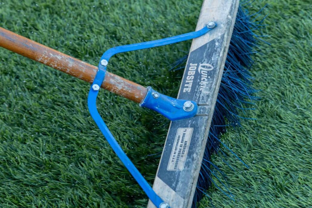 Close-up of a turf grooming brush on artificial grass treated with TurFresh, a non-toxic, eco-friendly turf cleaner that eliminates odors and is safe for pets and children.