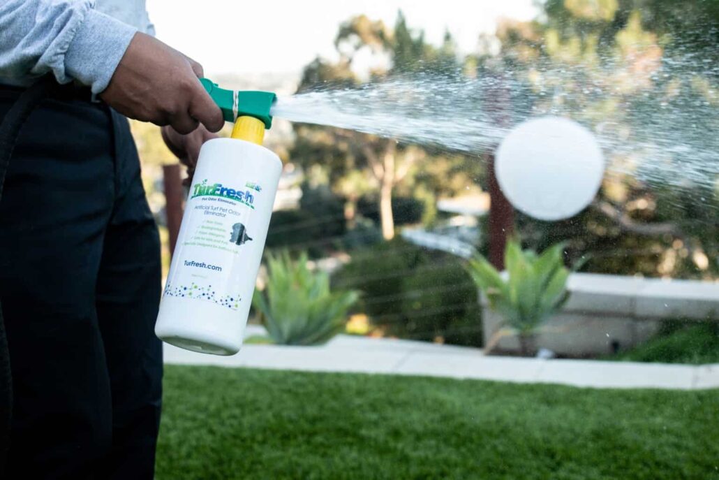 "Close-up of a person spraying TurFresh artificial turf cleaner, emphasizing its easy application, non-toxic formula, and eco-friendly effectiveness in eliminating pet odors from synthetic grass."
