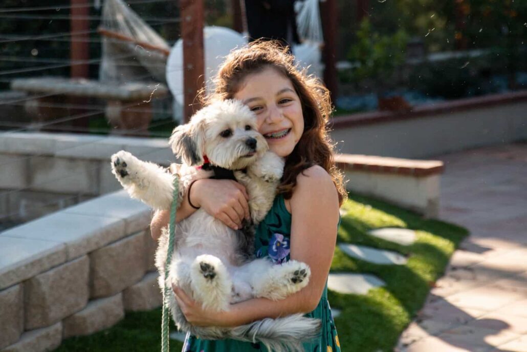 Smiling young girl holding her dog on a backyard lawn, highlighting TurFresh’s non-toxic, pet-safe, and eco-friendly turf cleaner that eliminates odors and keeps outdoor spaces fresh and safe for families.