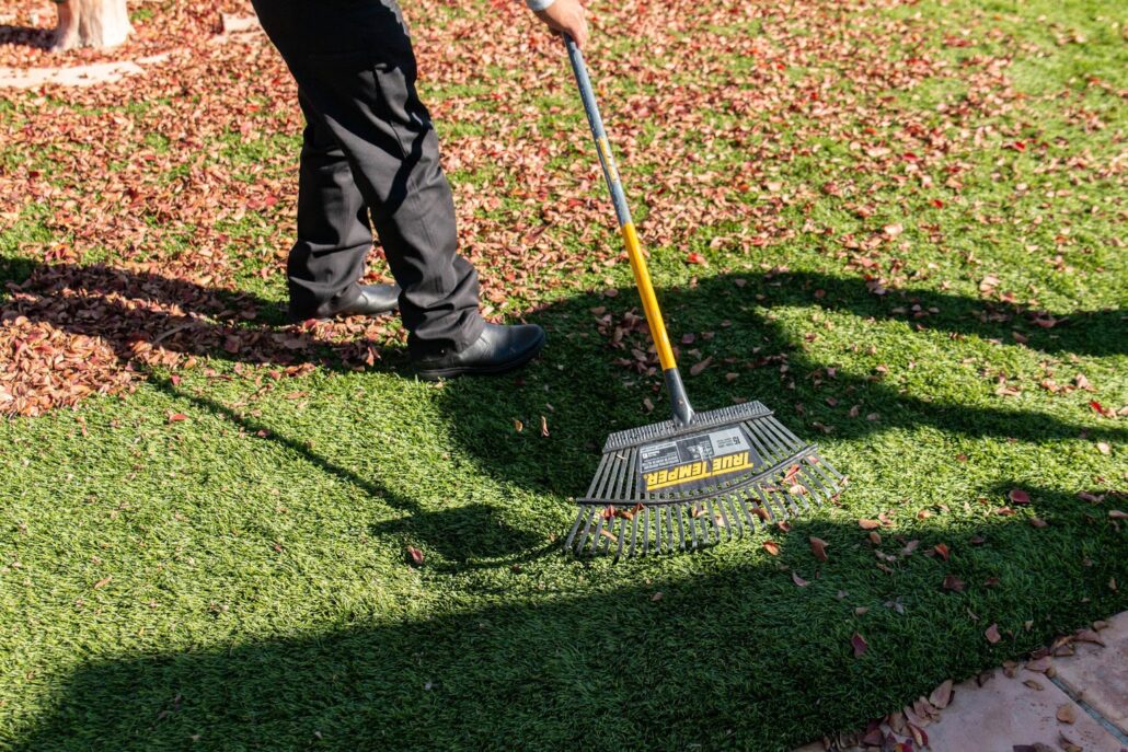 Worker raking leaves off artificial turf maintained with TurFresh, an eco-friendly, pet-safe turf cleaner that eliminates odors and keeps synthetic lawns fresh and clean.