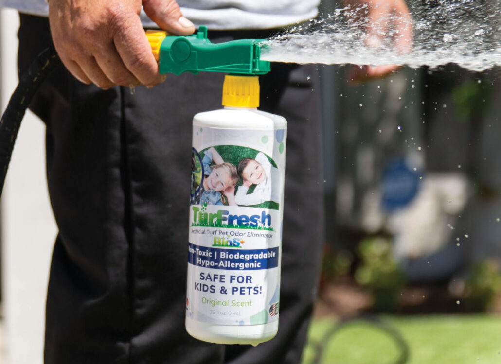 Close-up of TurFresh turf deodorizer being sprayed with a hose attachment, showcasing its non-toxic, biodegradable, and pet-safe formula designed to eliminate odors and keep artificial grass fresh and clean for kids and pets.