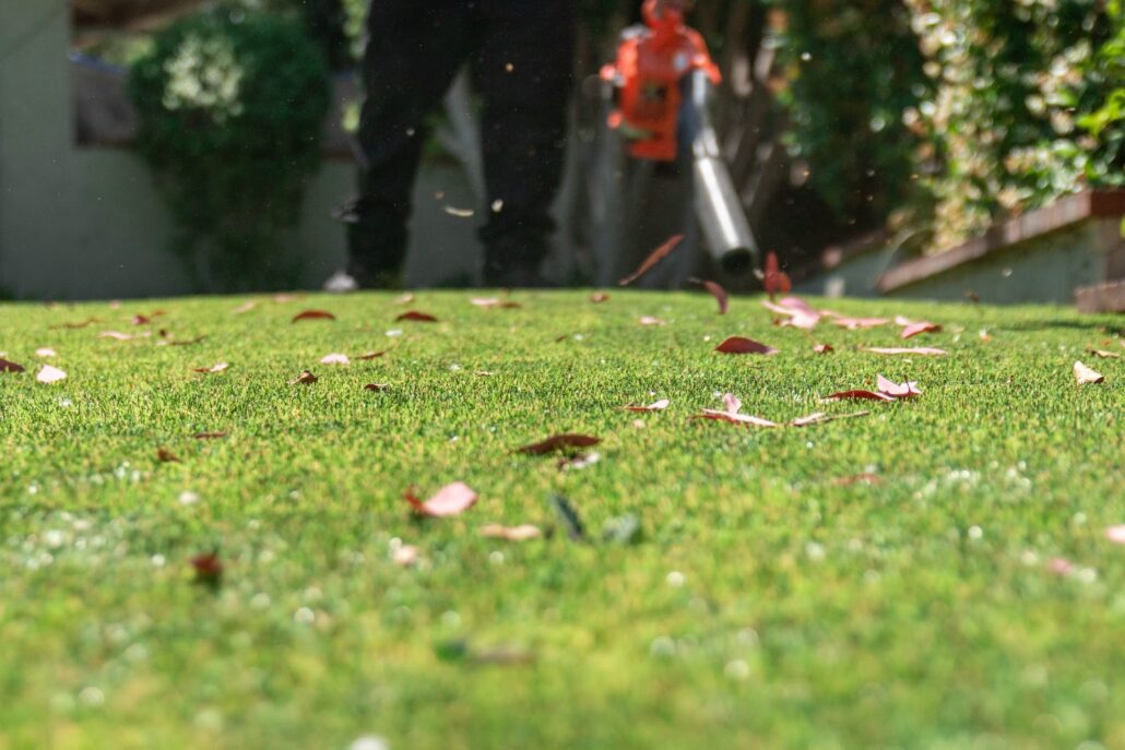 Close-up of artificial turf being cleared of leaves by a professional using a blower, with TurFresh keeping the surface fresh, odor-free, eco-friendly, and safe for pets and families.