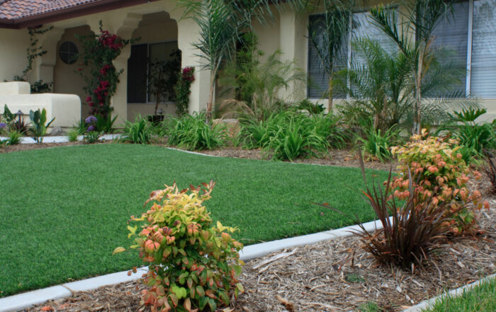 Front yard with lush green artificial turf lawn treated with TurFresh and surrounded by landscaped plants