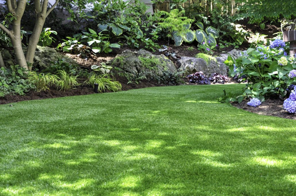 Lush artificial turf lawn surrounded by garden plants cleaned and maintained by TurFresh.