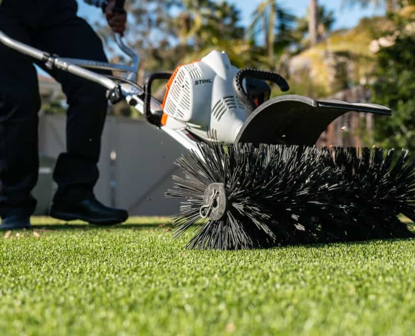 Artificial Turf Power Broom Cleaning for a Fresh, Clean Lawn Appearance Power broom being used to clean and refresh artificial turf for optimal appearance and drainage.