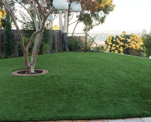 Low-Maintenance Backyard with Artificial Turf for Clean, Green Outdoor Living Backyard with artificial turf surrounding a tree, offering a neat and low-maintenance green space.