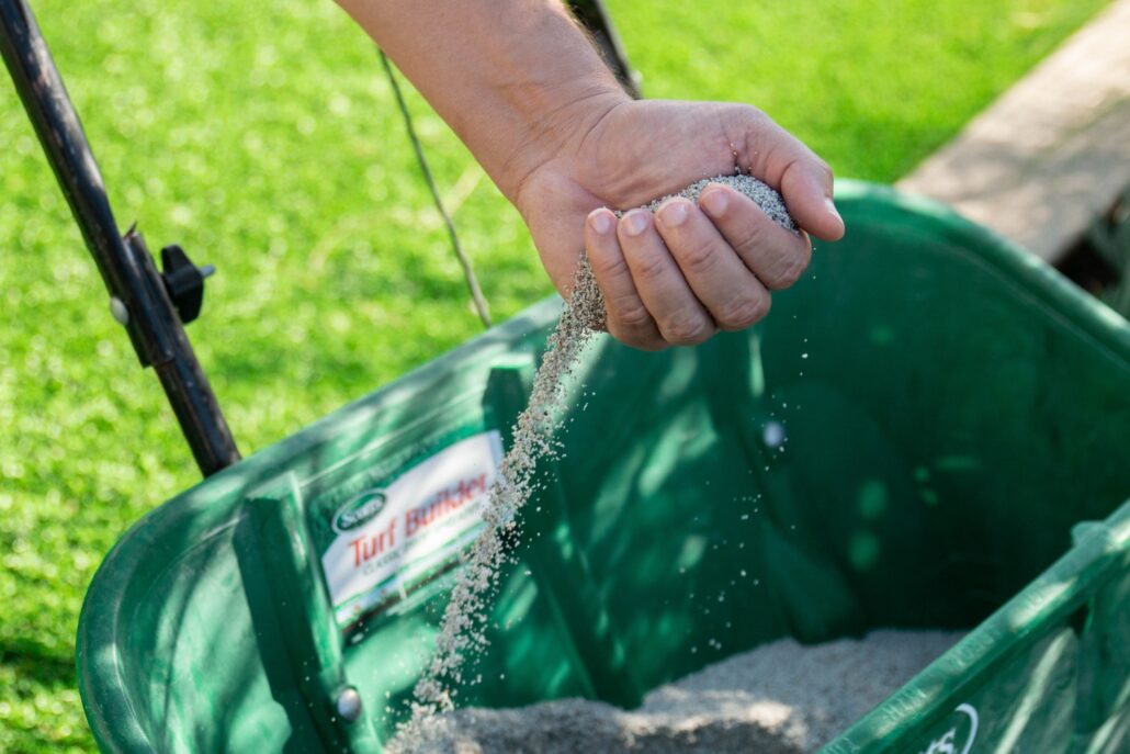 Hand pouring TurFresh artificial turf infill granules into green spreader for maintaining clean, fresh synthetic grass lawn