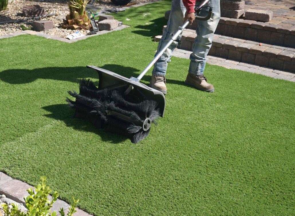 "Technician using a power brush to clean artificial turf, showcasing TurFresh’s professional-grade service that eliminates odors, is eco-friendly, and safe for pets and the environment."
