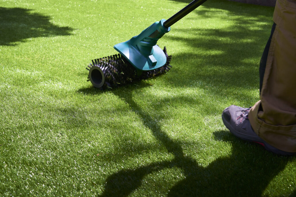 "Close-up of a TurFresh technician using a power brush on artificial turf, demonstrating eco-friendly, pet-safe cleaning that eliminates odors and restores synthetic grass to like-new condition."