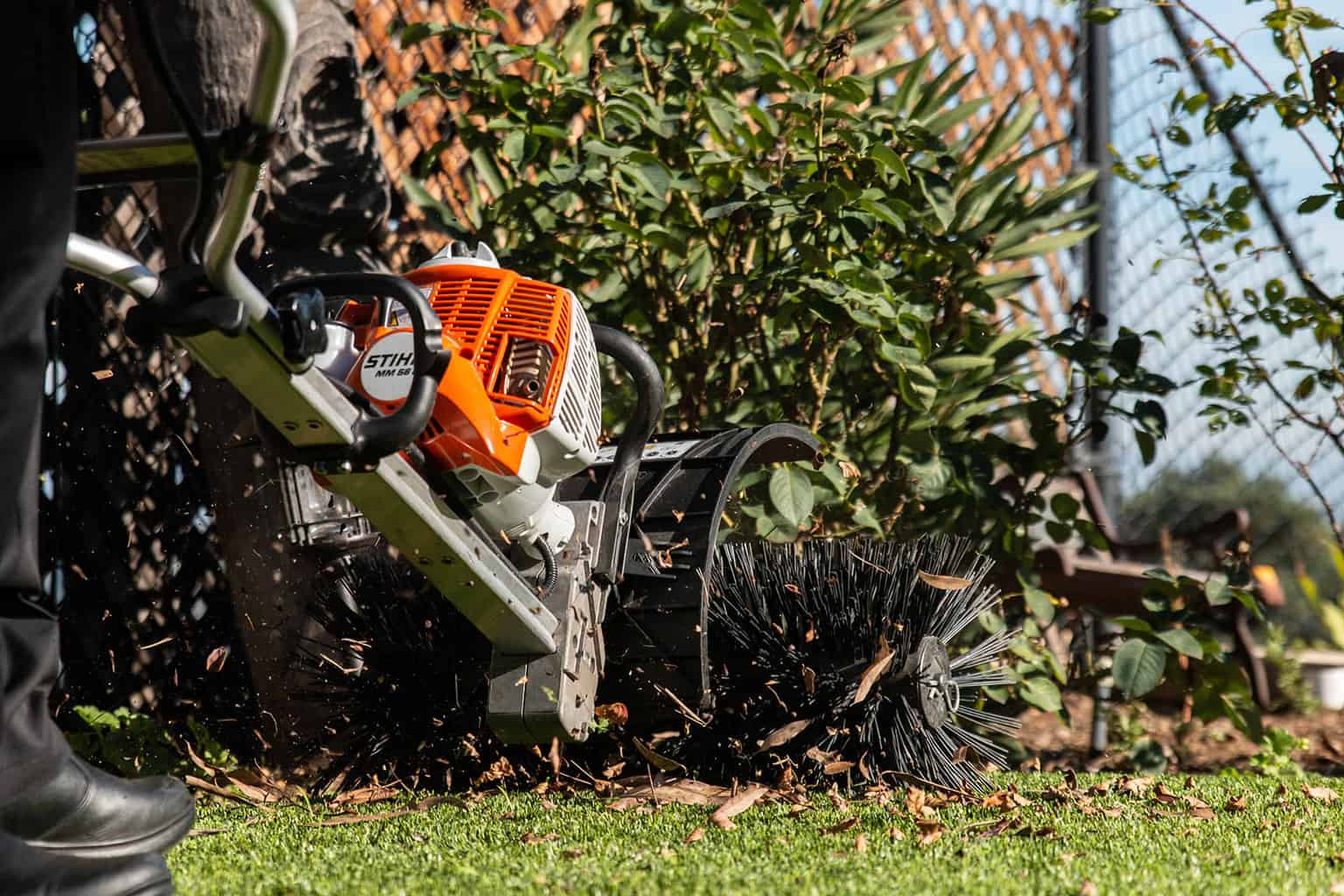 Artificial turf maintenance service brushing leaves from lawn Technician brushing synthetic turf lawn to remove leaves and debris