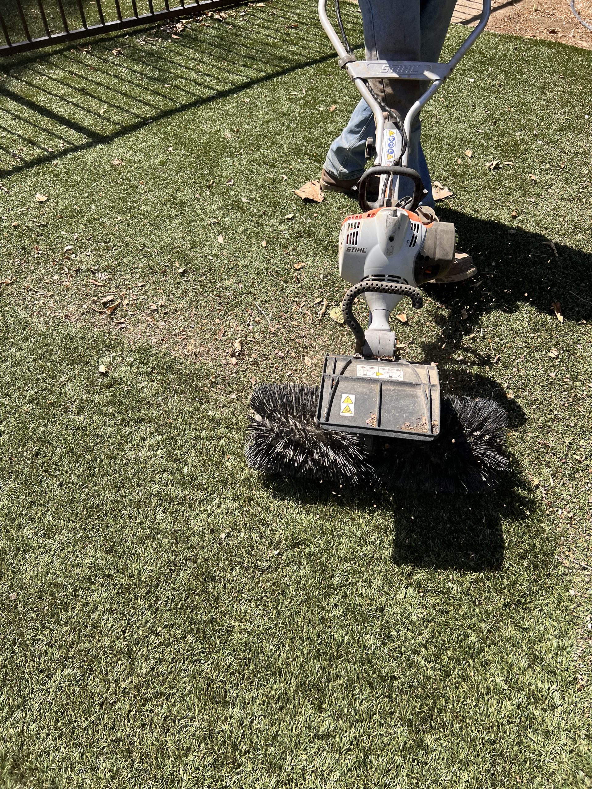Close-up of a TurFresh technician using a power brush on artificial turf, visibly lifting and revitalizing the fibers while removing debris—highlighting TurFresh’s pet-safe, eco-friendly formula that eliminates odors and restores turf appearance.