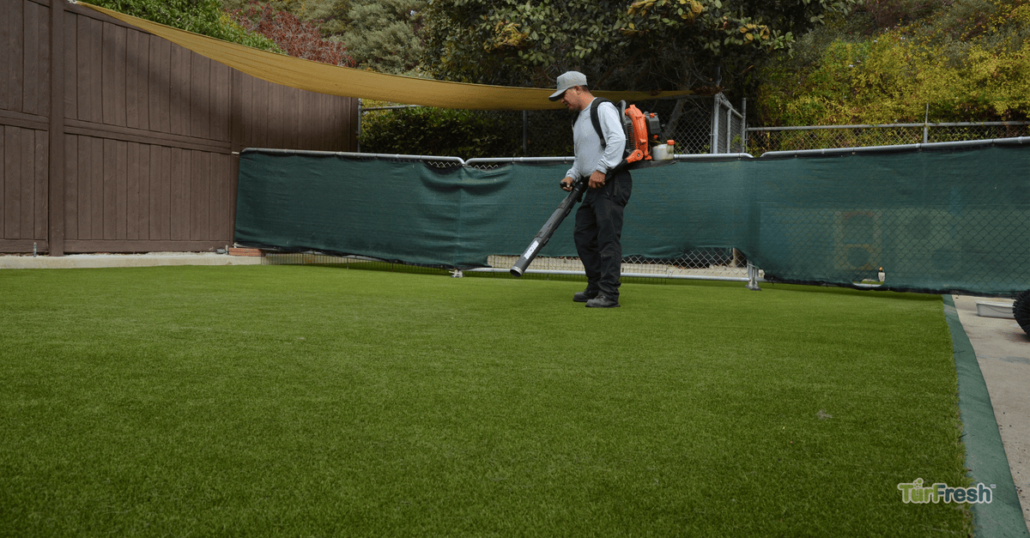 TurFresh technician using professional equipment to clean artificial turf in a residential or commercial yard, ensuring spotless and well-maintained synthetic grass.