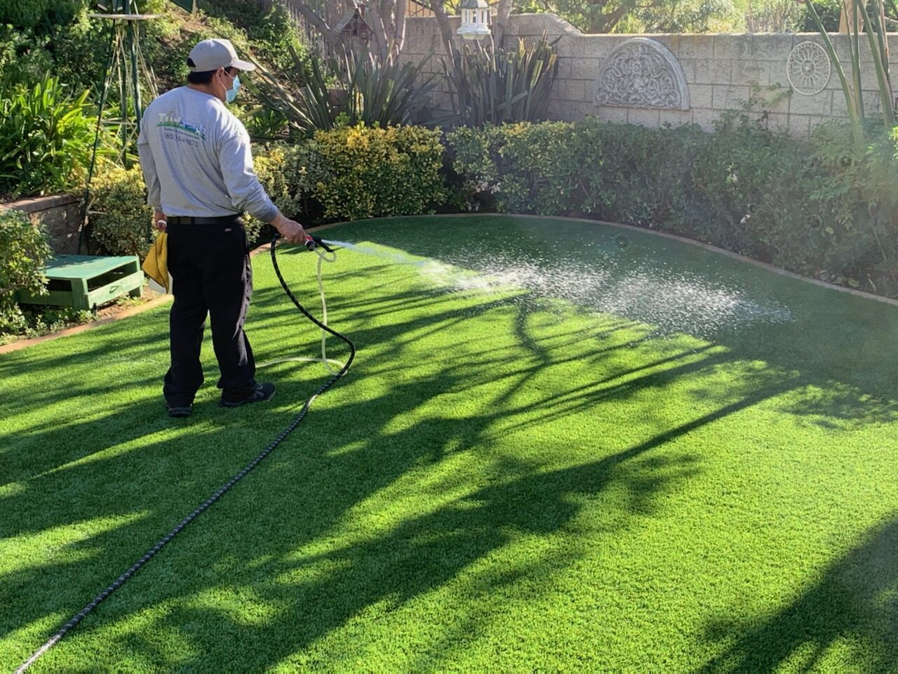 "Technician applying TurFresh cleaner to artificial turf in a backyard, showcasing its eco-friendly, non-toxic formula that eliminates odors and is safe for kids and pets."