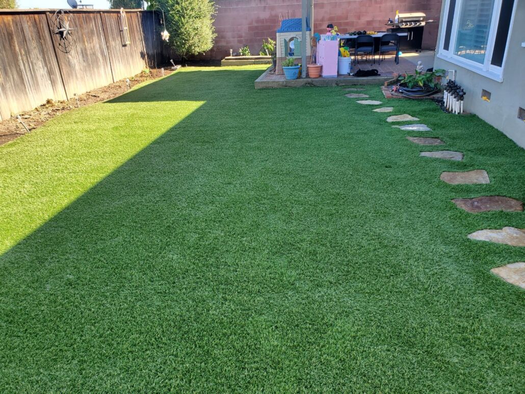 Backyard with clean, vibrant artificial grass treated with TurFresh, featuring a stone path and play area—highlighting the product’s eco-friendly, pet-safe formula that eliminates odors and keeps outdoor spaces fresh and family-ready.