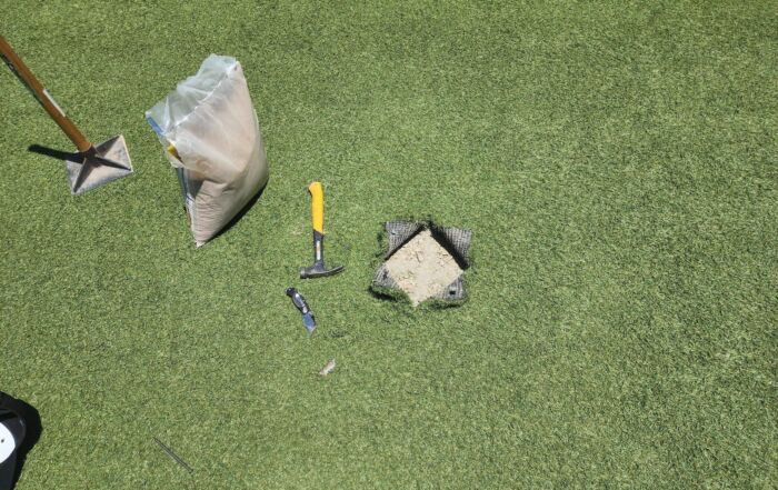 "Artificial turf maintenance with tools and infill shown during TurFresh application, a non-toxic, eco-friendly solution for eliminating odors and keeping turf fresh and safe for pets."