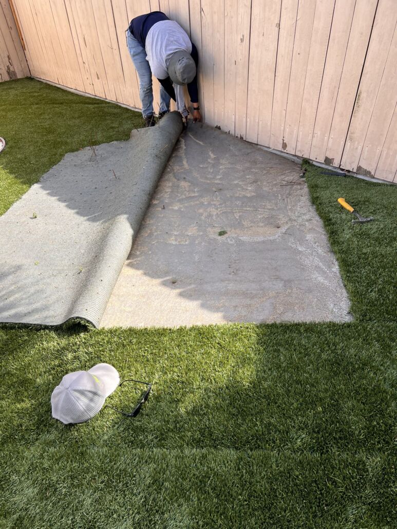 "Technician lifting artificial turf for deep cleaning and restoration using TurFresh, an eco-friendly, pet-safe solution that eliminates odors and revitalizes synthetic grass from the base up."