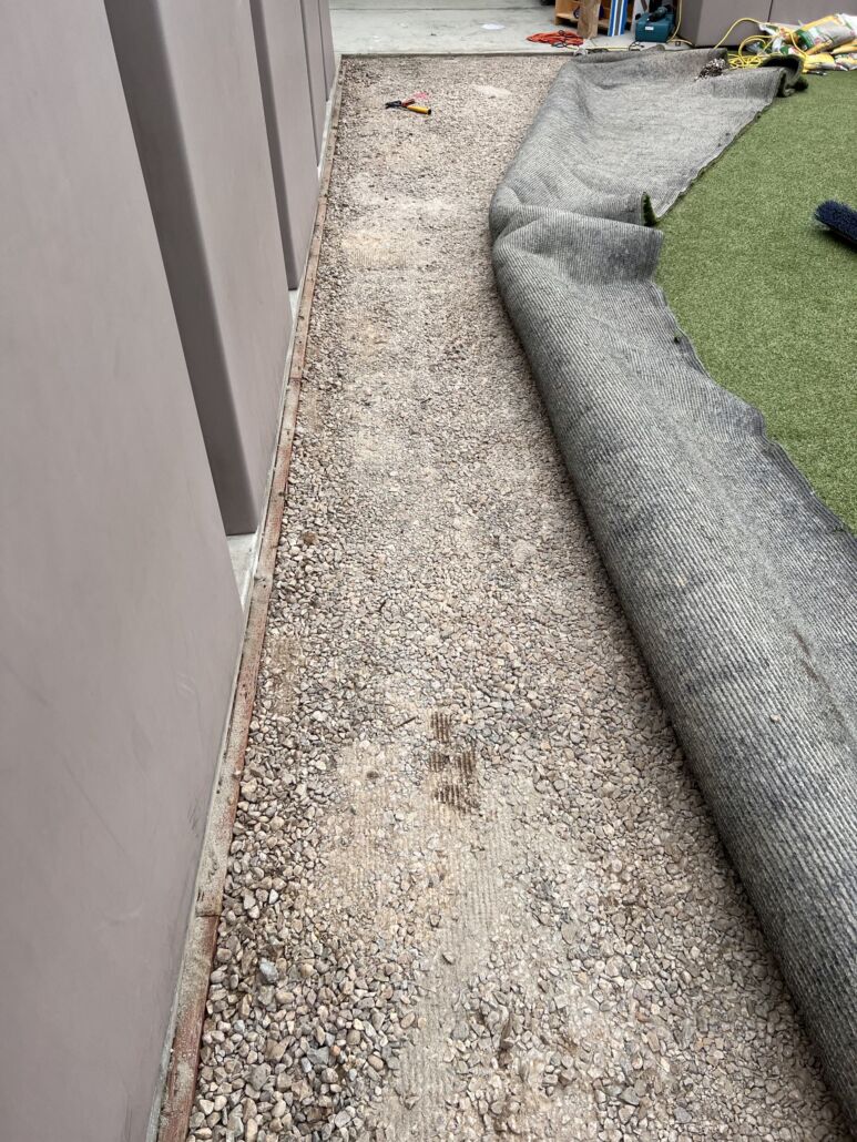 Partially lifted artificial turf exposing gravel sub-base during maintenance, highlighting TurFresh’s deep-cleaning and odor-eliminating services that are eco-friendly and safe for pets.
