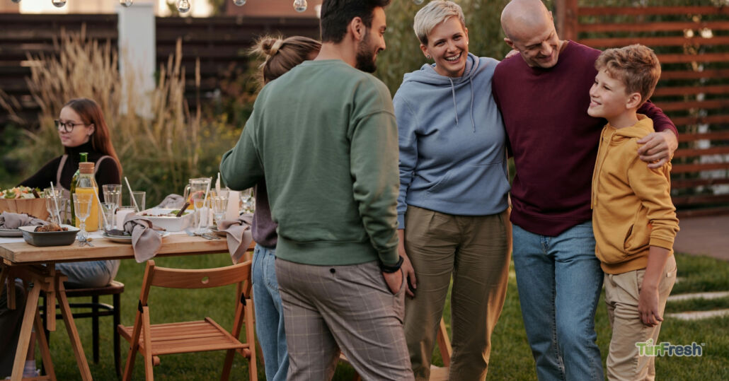 Happy family enjoying a backyard gathering on well-maintained artificial turf cleaned by TurFresh.