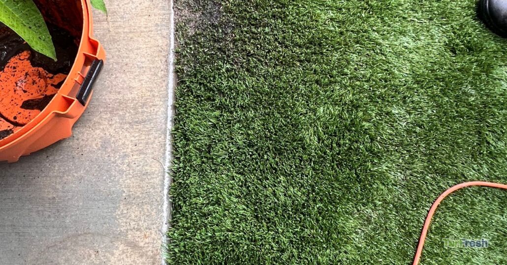 Close-up of artificial turf cleaned and restored by TurFresh, showing vibrant green blades next to a concrete edge.