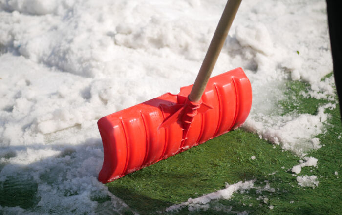 Clearing snow off artificial turf with a red shovel to maintain turf quality in winter — TurFresh maintenance tip.