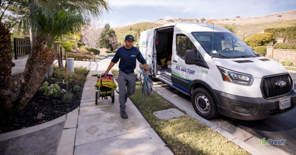 TurFresh technician arriving with equipment from branded service van for artificial turf cleaning and maintenance.
