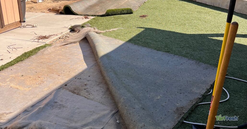Partially removed artificial turf during maintenance work with tools and debris visible.