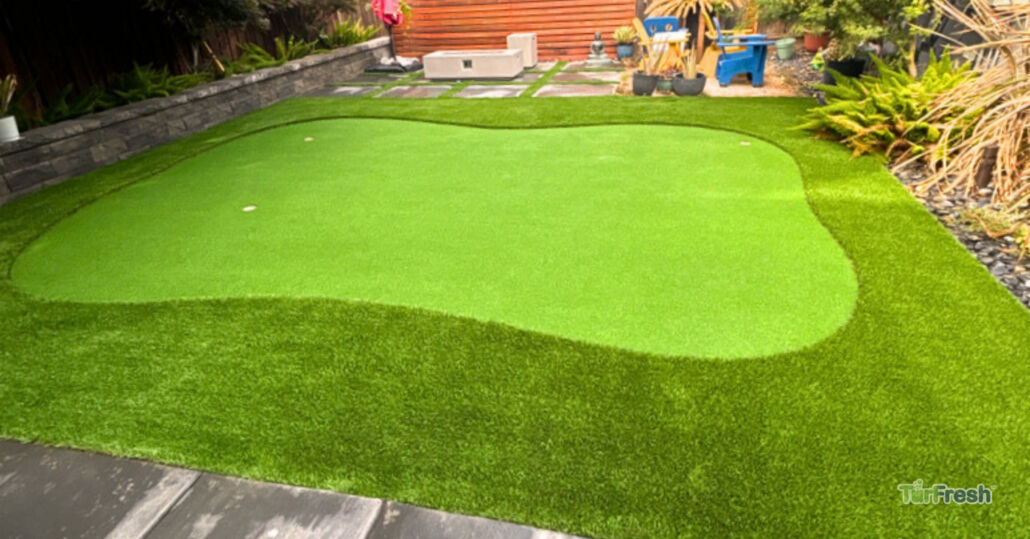 Clean and vibrant artificial turf backyard putting green surrounded by landscaping, maintained by TurFresh.