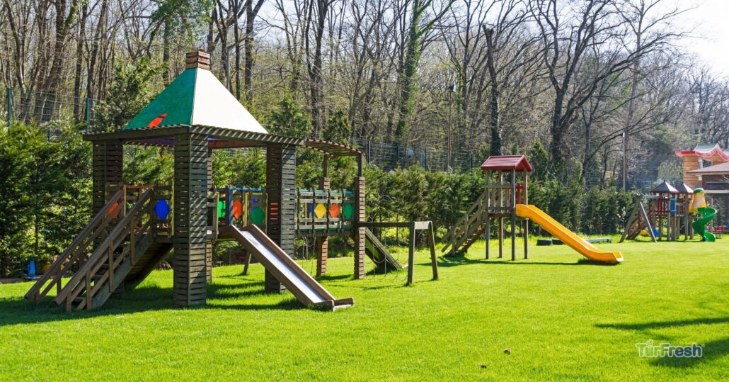 Clean artificial turf playground with wooden play structures and slides after TurFresh turf maintenance.