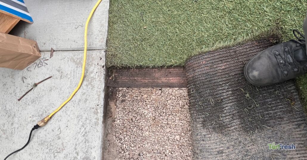 Close-up of artificial turf being lifted for maintenance, showing base layers and staples – TurFresh turf repair in progress.