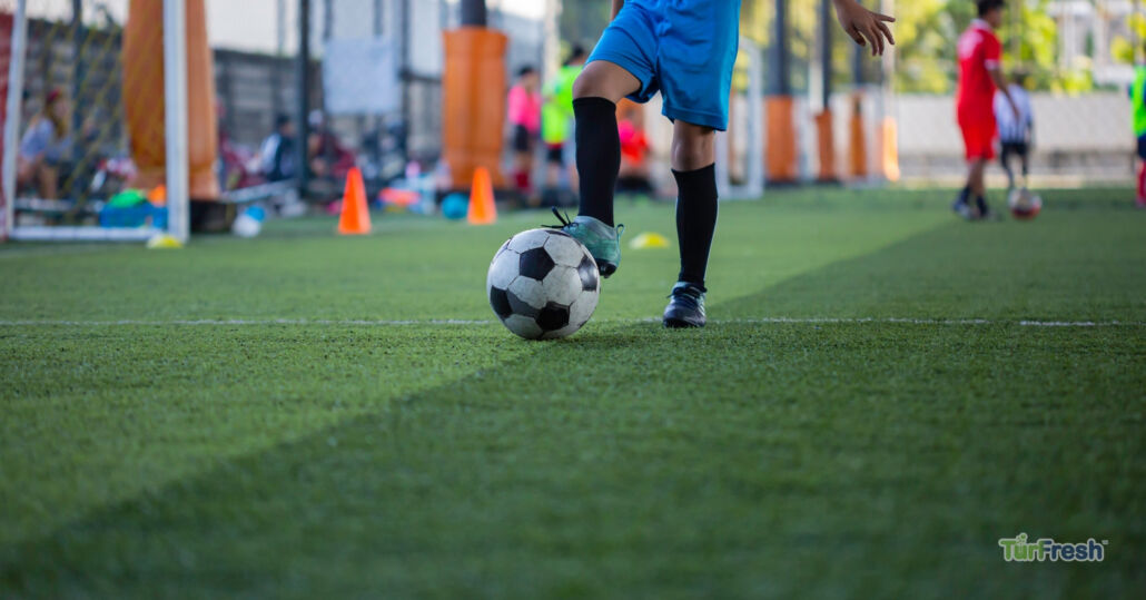 Youth soccer player on clean artificial turf field maintained with TurFresh sports turf cleaning products for safe play.