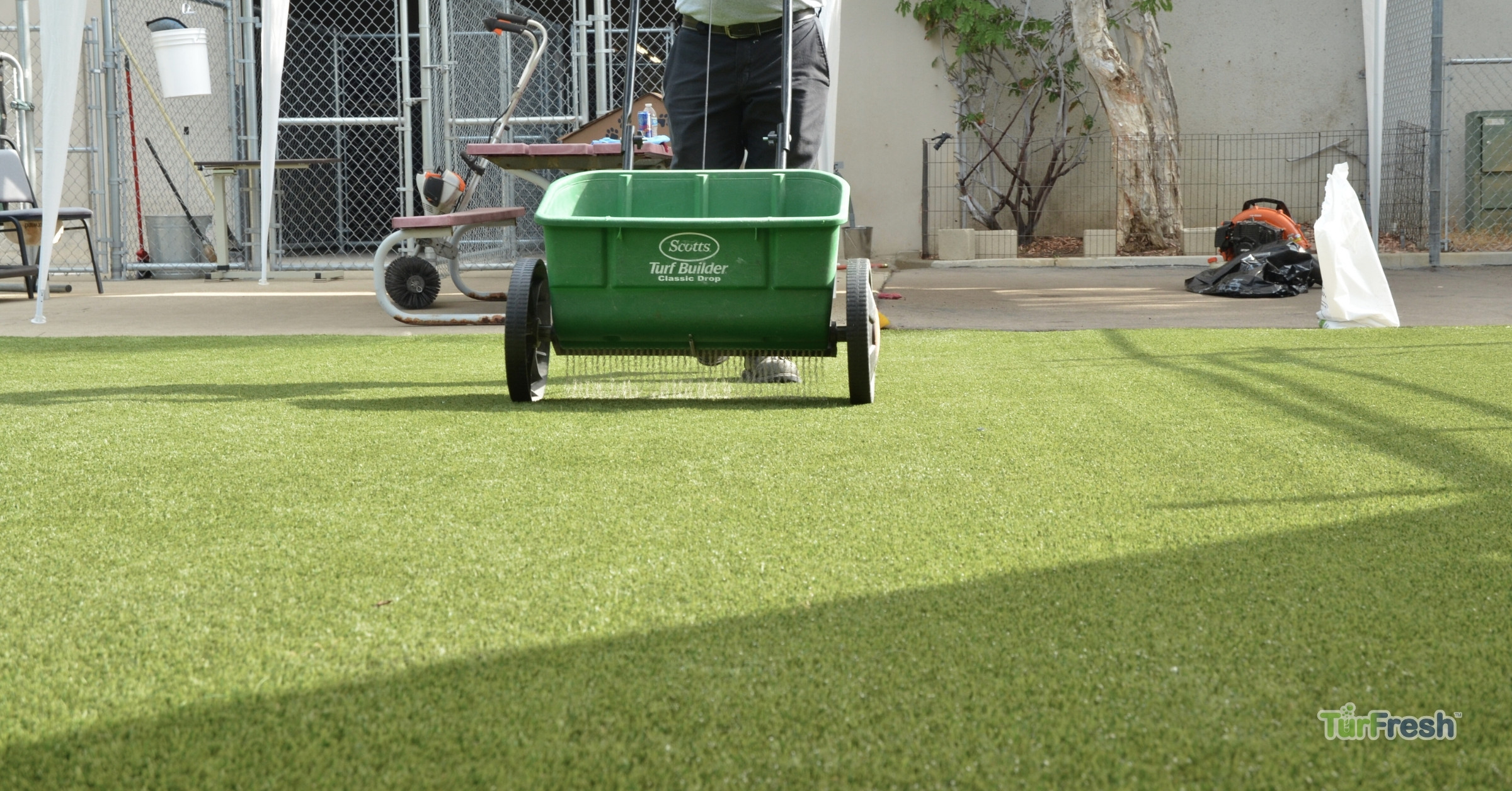 Artificial turf infill application by TurFresh for optimal lawn performance and appearance TurFresh technician applying infill with a drop spreader on a clean artificial turf surface.