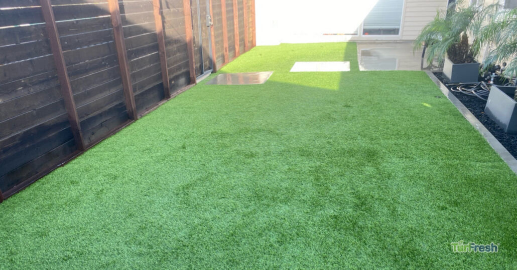 Clean artificial turf side yard along wooden fence with patio and planters, maintained by TurFresh.