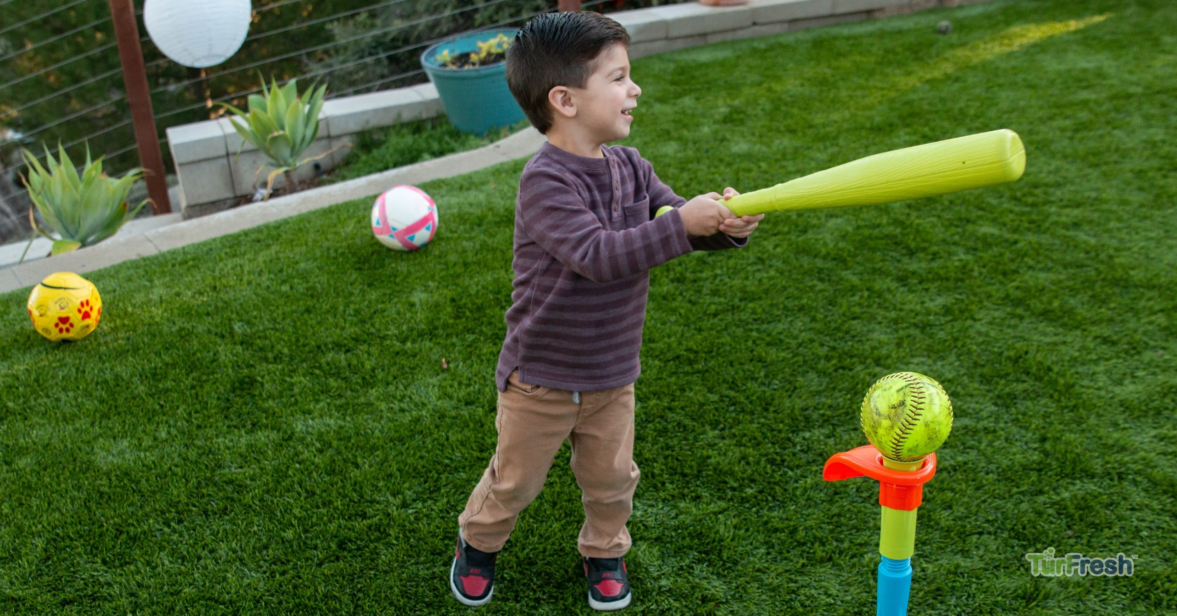 Child playing on TurFresh artificial turf backyard lawn Child playing tee ball on TurFresh artificial turf backyard lawn with toys and safe green grass