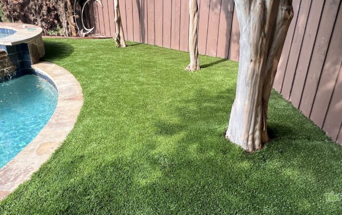 Artificial turf lawn around a backyard pool and trees, freshly cleaned and maintained by TurFresh.