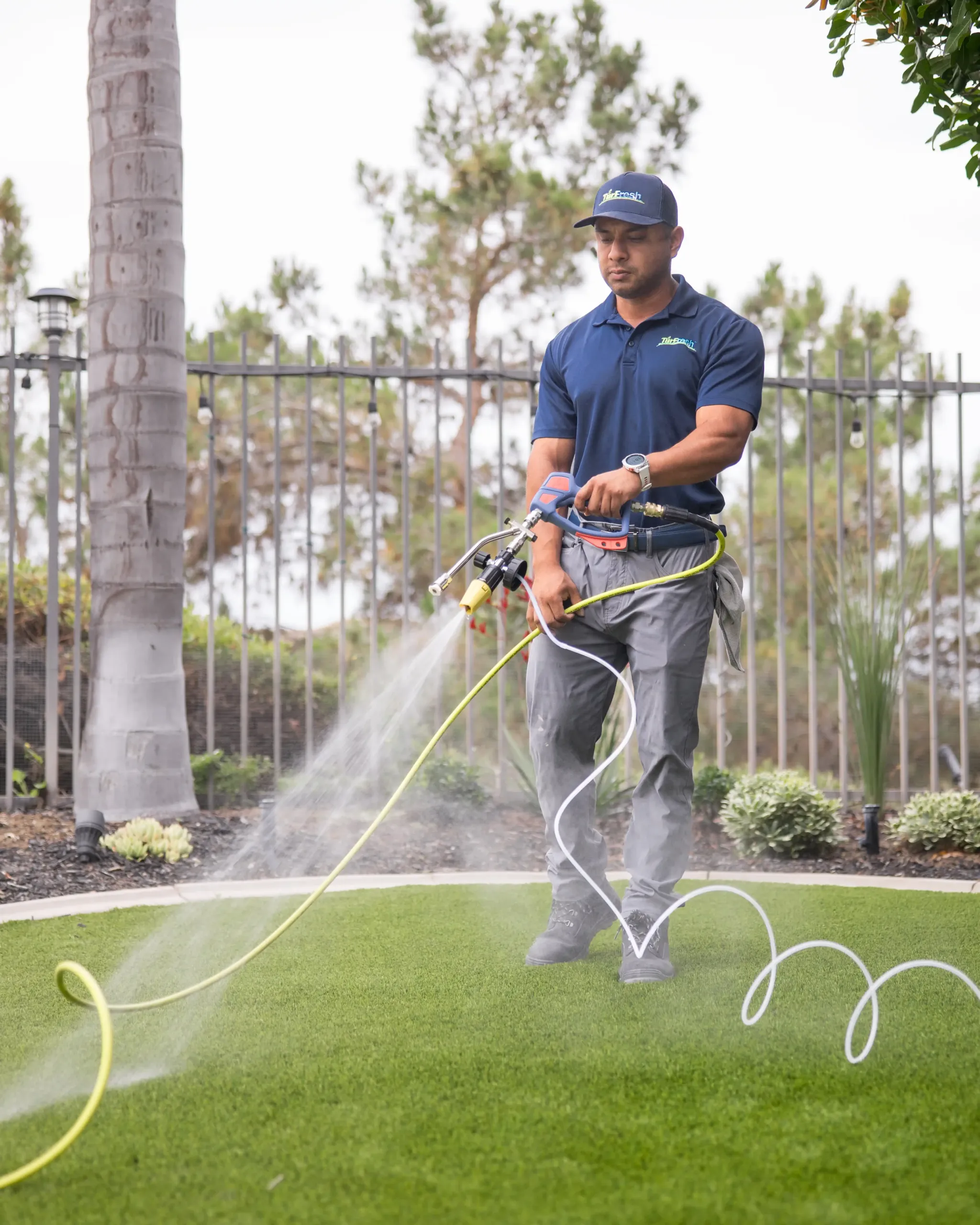 TurFresh technician spraying cleaner on artificial turf backyard lawn TurFresh technician spraying cleaner across artificial turf backyard lawn to sanitize, deodorize, and refresh synthetic grass.