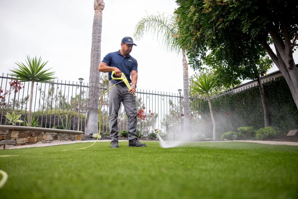TurFresh technician pressure washing artificial turf in a residential backyard to deep clean and deodorize the synthetic grass.