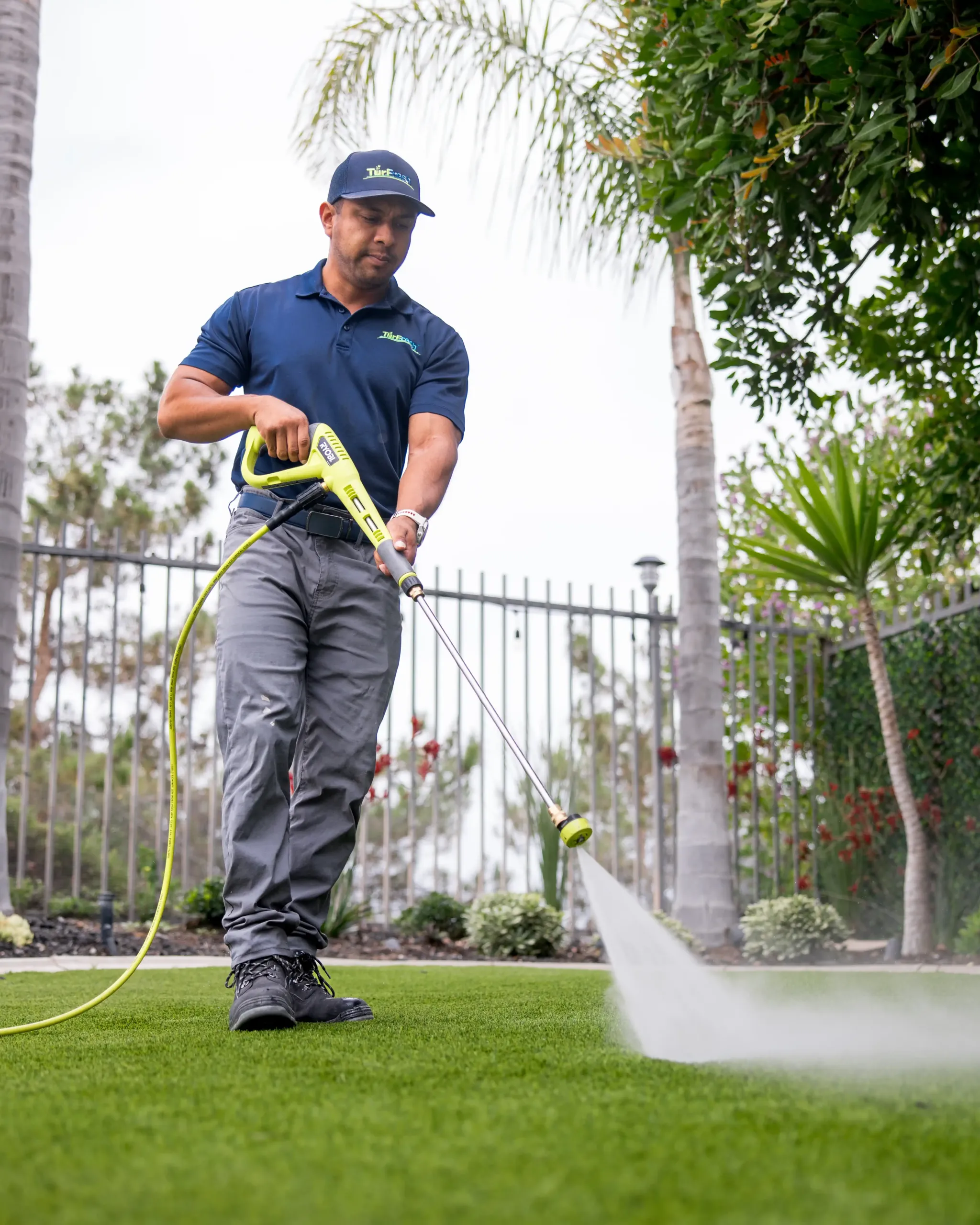 Synthetic Turf Cleaning Service by Technicians Technician power-washing synthetic turf for maintenance service