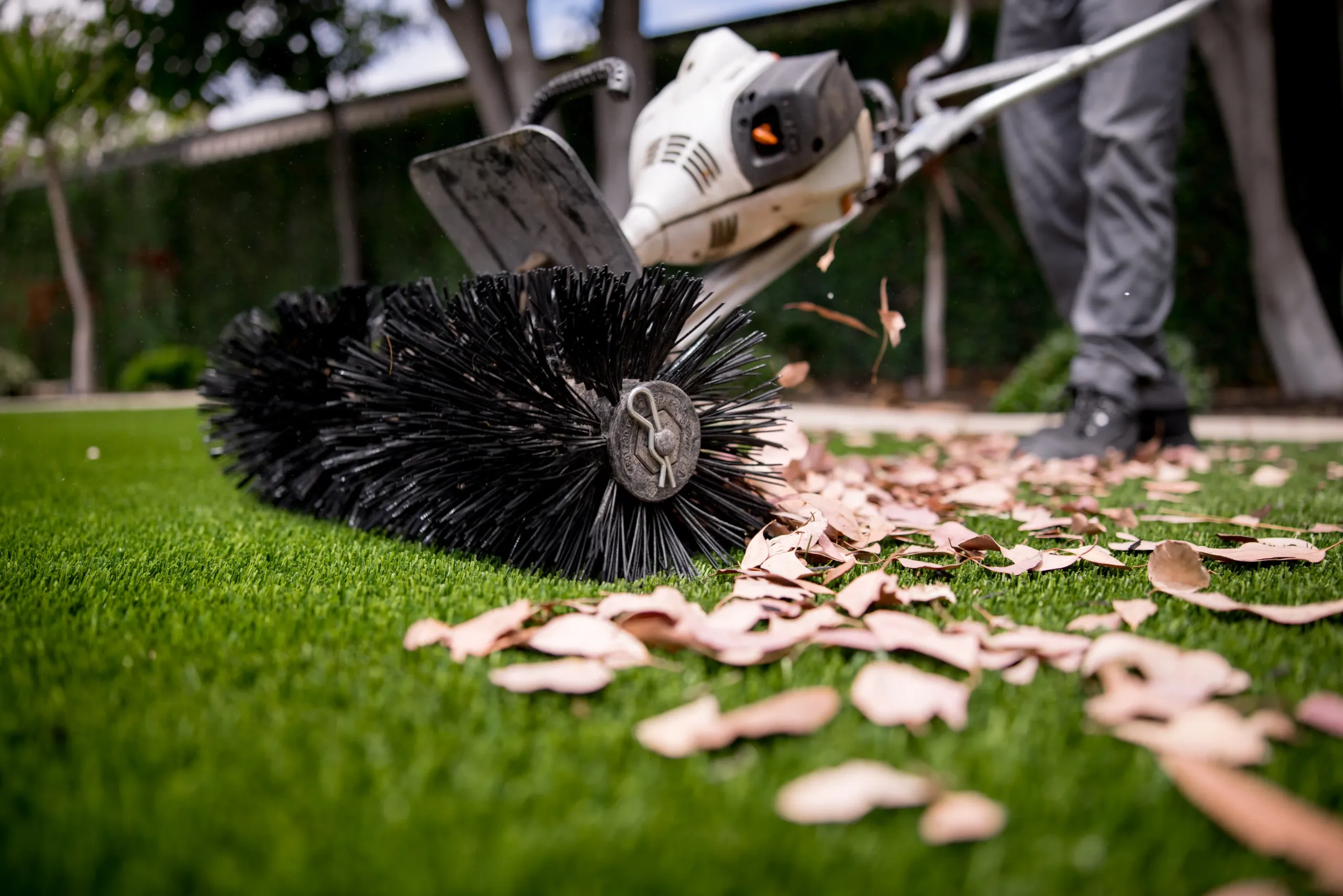 Artificial Turf Maintenance Leaf Removal Service Technician brushing synthetic turf to clear leaves and debris
