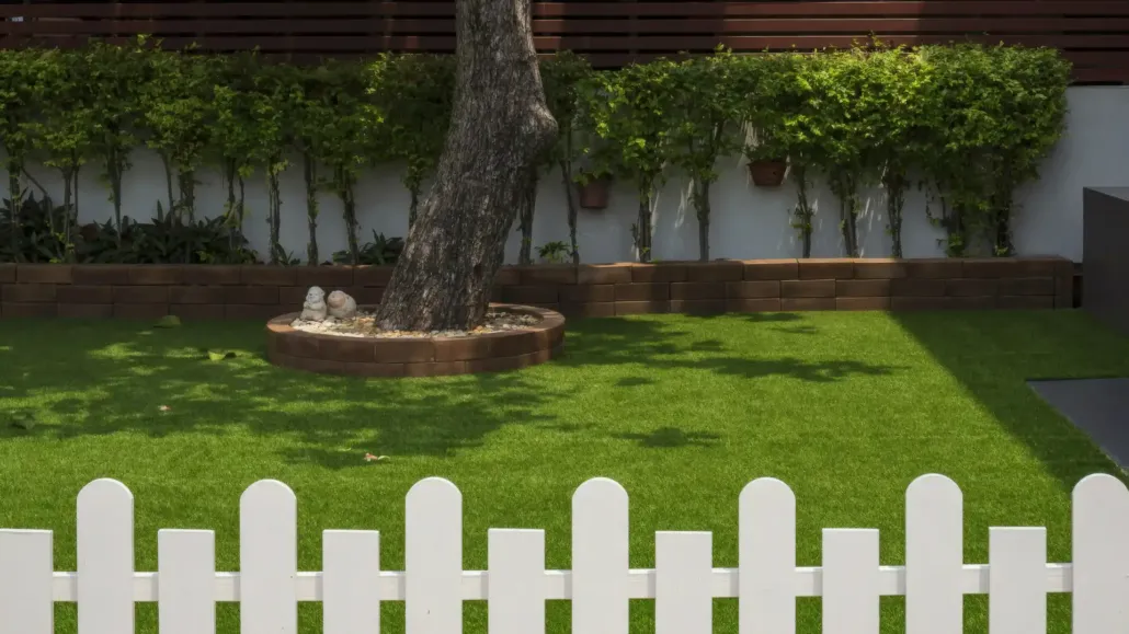 Neat backyard with white picket fence and bright artificial turf lawn kept clean and fresh using TurFresh maintenance products.