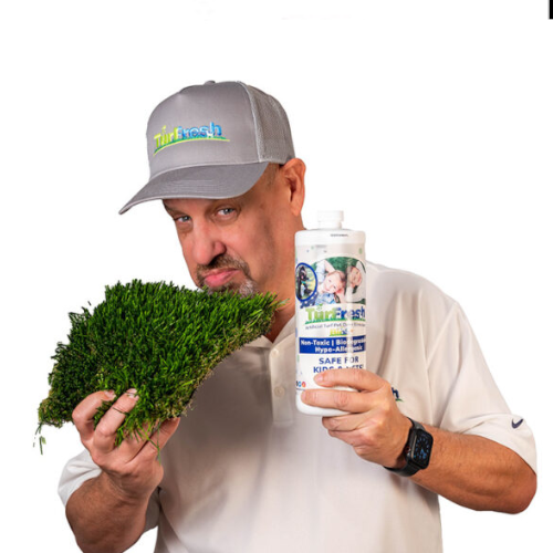 TurFresh expert demonstrating artificial turf odor removal cleaner TurFresh Owner Jhon Pla smelling a piece of artificial turf while holding TurFresh cleaner to show fresh, odor free synthetic grass care.